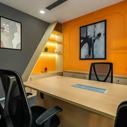 Small office with a wooden desk, black chairs and an orange wall